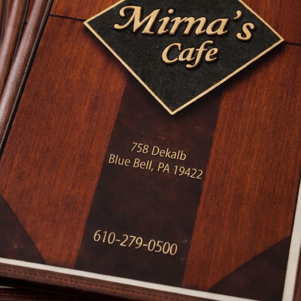 Mirna’s Cafe menu displaying its name, Blue Bell, Pennsylvania address, and phone number on a wooden tabletop.